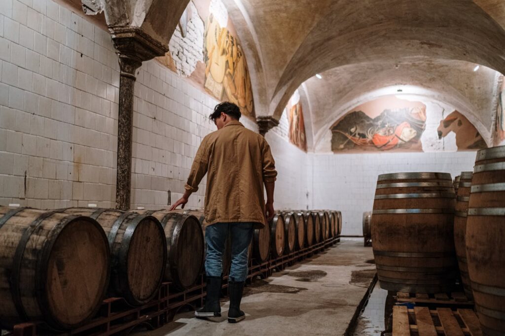 A man inspecting wooden barrels in a brewery cellar, checking fermentation storage.