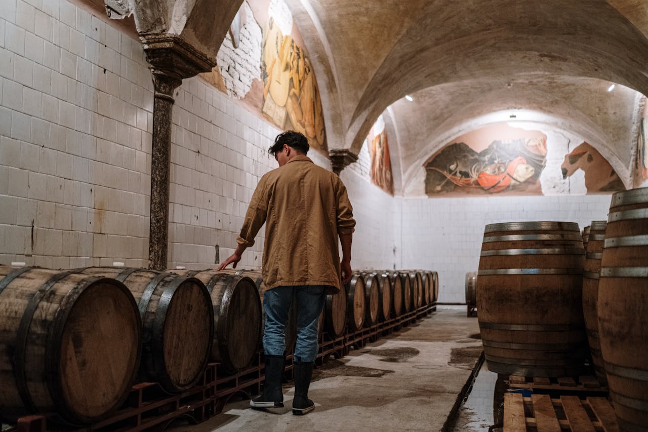 A man inspecting wooden barrels in a brewery cellar, checking fermentation storage.