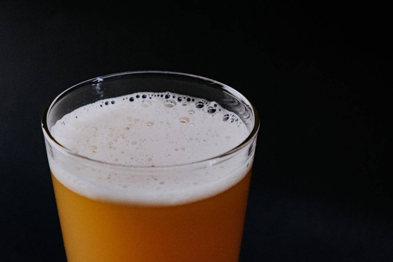 A detailed close-up of a frothy beer glass against a black background, highlighting the foam and bubbles.